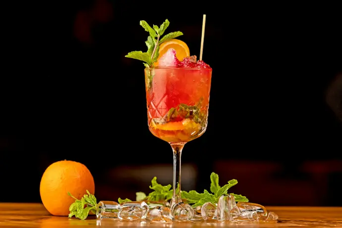 a glass filled with a drink next to an orange